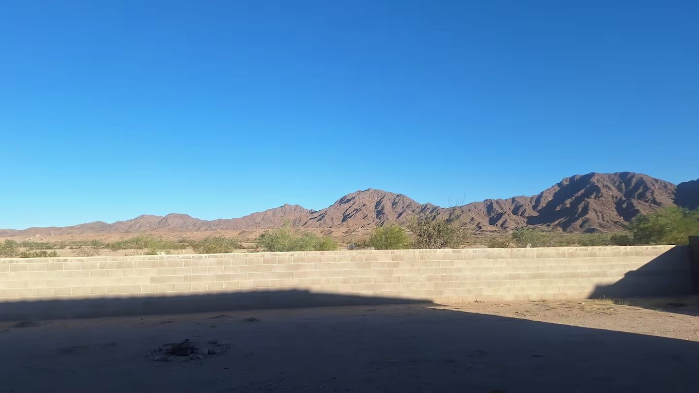 A desert landscape with mountains in the background and a concrete wall in the foreground.