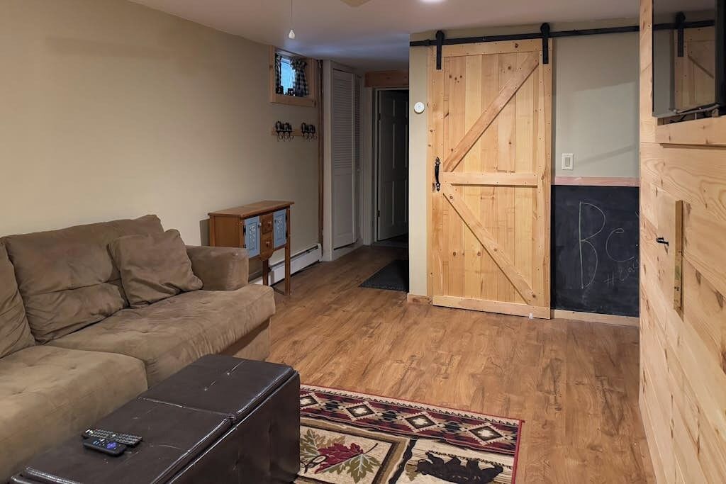 Een woonkamer met een bank, een salontafel, een houten deur en een vloerkleed met een patroon.