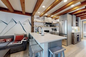 Eine moderne Küche mit Kochinsel, Holzbalken an der Decke und einer Couch mit einem Sitzkissen im Ski-Design.