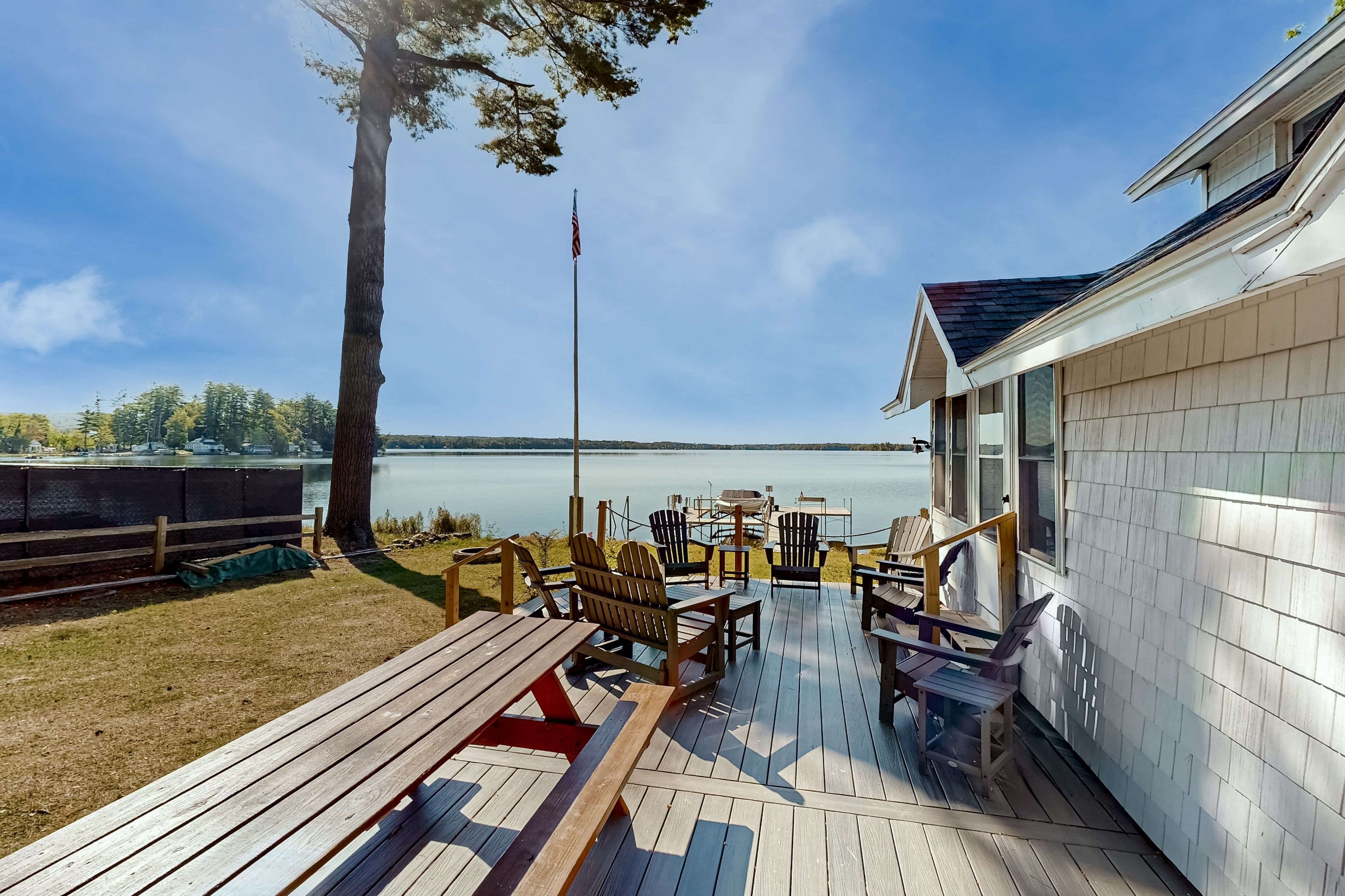 A wooden deck with Adirondack chairs, a picnic table, and a view of a lake.