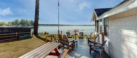 Una terraza de madera con sillas Adirondack, una mesa de picnic y vistas a un lago.
