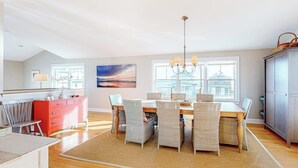 Uma sala de jantar com mesa, cadeiras, um candelabro e vista da cidade por grandes janelas.
