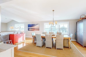 A dining area with a table, chairs, a chandelier, and a view of the city through large windows. - Lovely oceanfront home with balcony, central AC, & washer/dryer (Wells)