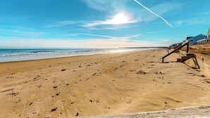Uma praia com um calçadão de madeira que leva a um prédio com varanda.