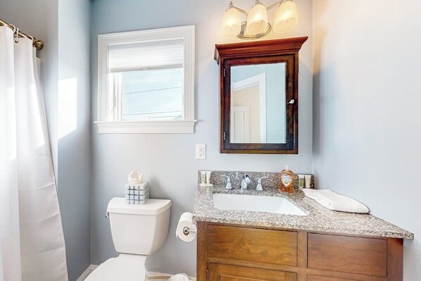 A bathroom with a white toilet, a sink with a wooden vanity, a mirror above the sink, and a window with a white blind.