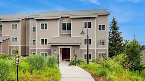 A multi-story residential building with a central entrance, a small porch, and a pathway leading to the entrance.