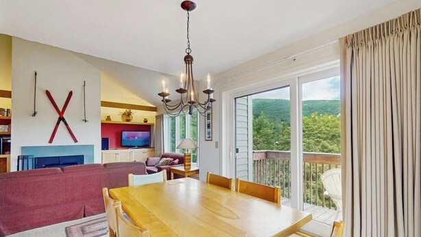 A dining area with a wooden table and chairs, a chandelier, and a television in the background.