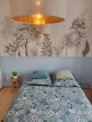 A bedroom with a floral-patterned bedspread, a wall-mounted lamp, and a tree mural. - Bright Room - Centre (Lourdes)