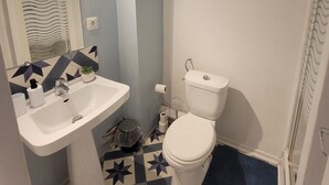 Kylpyhuone, jossa on valkoinen pesuallas, wc ja kuviollinen lattia.