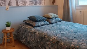 Makuuhuone, jossa on kukallinen päiväpeite sängyllä, seinään kiinnitetty lamppu ja ikkuna, jossa on verhot.
