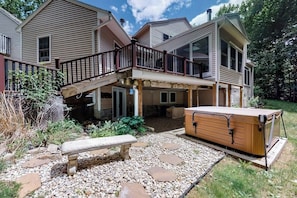 Ein zweistöckiges Haus mit überdachter Terrasse, Whirlpool und einem Kiesweg.