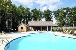 A swimming pool with lounge chairs, a small building with a porch, and trees in the background.