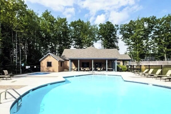 A swimming pool with lounge chairs, a small building with a porch, and trees in the background.