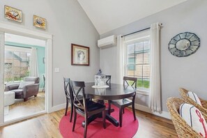 A dining area with a round table, four chairs, a red rug, and a large window with curtains.