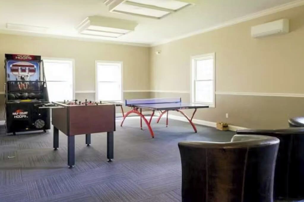 A room with a foosball table, ping pong table, and a pool table.