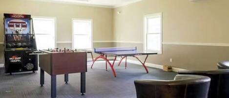 A room with a foosball table, ping pong table, and a pool table.
