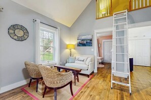 A living room with a sofa, two wicker chairs, a table, a lamp, a painting, and a ladder.