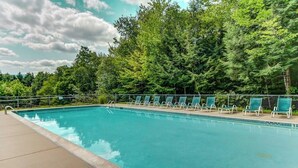 A swimming pool with lounge chairs and a forest backdrop.