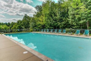 Une piscine avec des chaises longues et une forêt en arrière-plan.