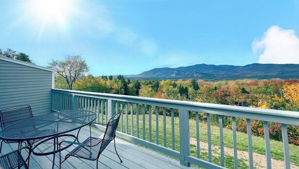 A deck with a table and chairs, overlooking a mountainous landscape with autumn foliage.