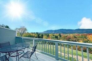 A deck with a table and chairs, overlooking a mountainous landscape with autumn foliage. - Scenic year-round retreat with amazing mountain views & tennis courts (Bartlett)
