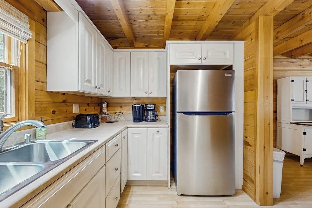 Una cocina compacta con armarios blancos, un refrigerador de acero inoxidable y techo de madera.