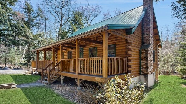 A log cabin with a porch, a chimney, and a small deck.