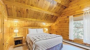 A wooden cabin bedroom with a bed, nightstands, and a window.