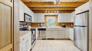 A modern kitchen with white cabinets, stainless steel appliances, and a wooden ceiling.