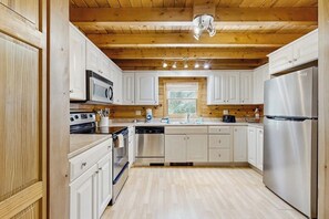 A modern kitchen with white cabinets, stainless steel appliances, and a wooden ceiling. - Charming Log Cabin w/ Free WiFi plus a Community Pool, Tennis, & Clubhouse (Bridgton)