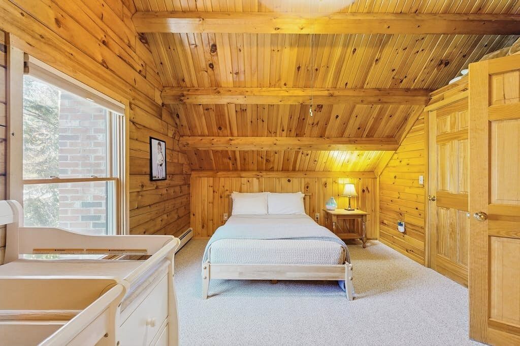 Una habitación con paneles de madera, una cama, una mesita de noche, una lámpara y una ventana.