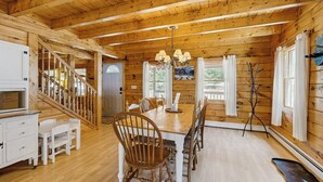 A wooden cabin interior with a dining table, chairs, a chandelier, and a staircase.