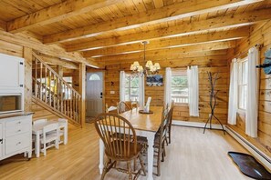 A wooden cabin interior with a dining table, chairs, a chandelier, and a staircase. - Charming Log Cabin w/ Free WiFi plus a Community Pool, Tennis, & Clubhouse (Bridgton)