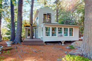 A two-story house with a balcony, surrounded by trees. - Togus Pond lakefront home with decks, canoe and firepit (Augusta)