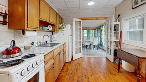 A kitchen with wooden cabinets, a stove, and a dining area with a table and chairs. - Entire lakefront home on Togus Pond with decks, canoe, firepit & great view (Augusta)