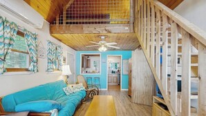 A cozy interior with a wooden staircase, a blue sofa, a wooden table, and a kitchen area.