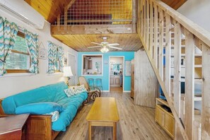 A cozy interior with a wooden staircase, a blue sofa, a wooden table, and a kitchen area. - Rustic lakefront cabin w/gas grill, firepit, kayaks, one canoe, A/C - 2 dogs OK (Leeds)