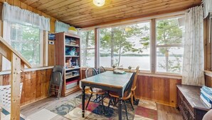 A wooden-paneled room with a dining table, chairs, a bookshelf, and large windows.