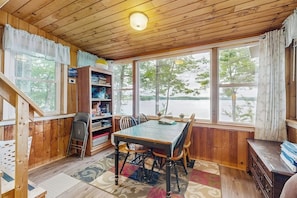 A wooden-paneled room with a dining table, chairs, a bookshelf, and large windows. - Rustic lakefront cabin w/gas grill, firepit, kayaks, one canoe, A/C - 2 dogs OK (Leeds)