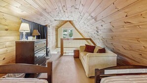 A cozy attic bedroom with wooden walls, a bed, a desk, and a window.