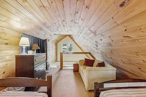 A cozy attic bedroom with wooden walls, a bed, a desk, and a window. - Rustic lakefront cabin w/gas grill, firepit, kayaks, one canoe, A/C - 2 dogs OK (Leeds)