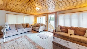 A living room with a wooden ceiling, two sofas, a fan, and a rug.