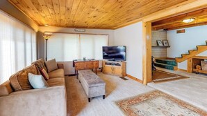 A cozy living room with a wooden ceiling, a sofa, a TV, and a staircase leading to another level.