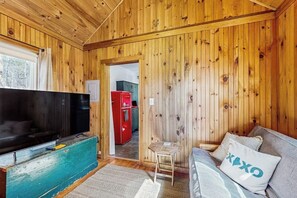 Una habitación con paneles de madera, un televisor, un refrigerador rojo, una mesita y un sofá con un cojín.