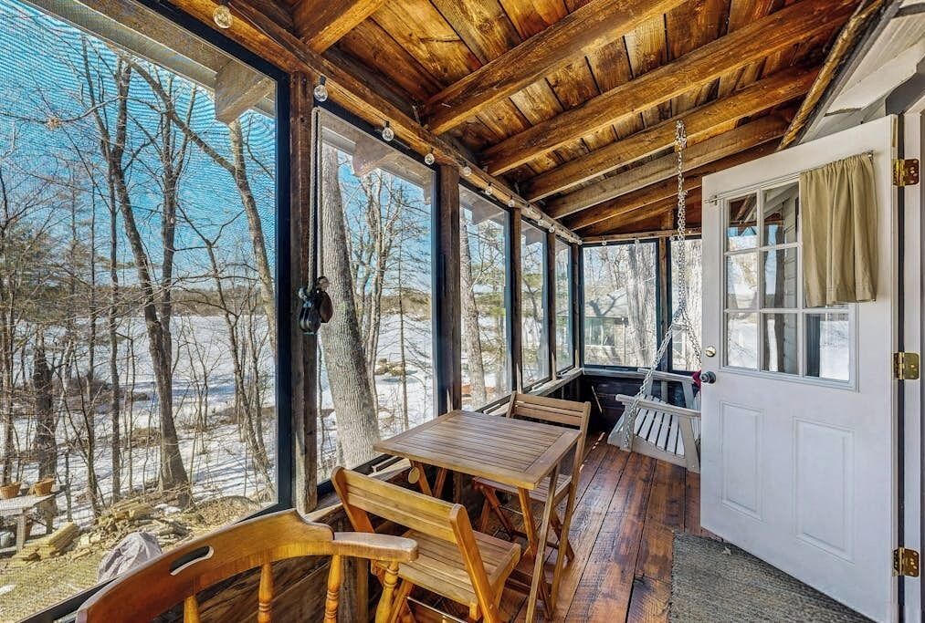 Una terraza de madera con una mesa, sillas, ventanas grandes y una puerta.