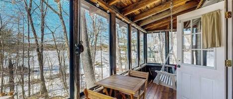 Una terraza de madera con una mesa, sillas, ventanas grandes y una puerta.