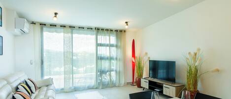 A modern living room with a sofa, a dining table set for two, a TV, and a surfboard.