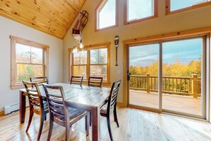 Ein Essbereich mit Holztisch und Stühlen, großen Fenstern und Blick auf eine Terrasse.