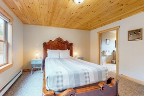 Ein Schlafzimmer mit Holzbalkendecke, einem Bett mit Kopfteil, Nachttischen, einem Beistelltisch, einem Spiegel und einem Fenster.