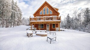 Una cabaña de troncos con balcón, rodeada de árboles cubiertos de nieve.